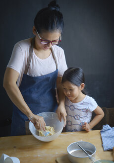 Mutter bringt ihrer Tochter bei, in einer Schüssel in der Küche Teig zu mischen - CAVF57284
