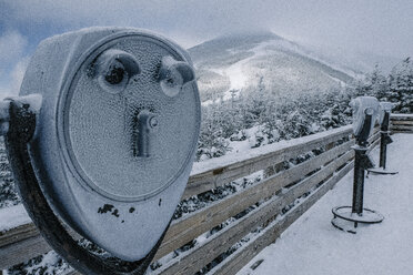 Snow covered coin-operated binoculars against mountains at observation point - CAVF57289