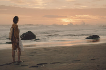 Side view of woman standing at beach against sky during sunset - CAVF57295