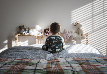 Rear view of boy sitting on bed at home - CAVF57307
