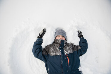 Draufsicht auf einen verspielten Jungen, der einen Schneeengel macht, während er im Winter spielt - CAVF57313