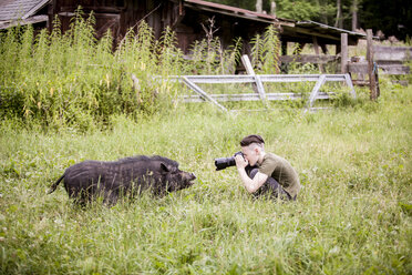 Side view of teenage boy photographing wild boar - CAVF57331