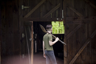 Jugendlicher, der eine Schaufel hält und an einer Holzhütte steht - CAVF57335