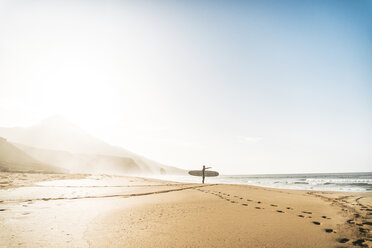 Man with surfboard standing on shore at beach against sky during foggy weather - CAVF57366