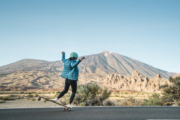 Rückansicht einer Frau, die einen Stunt auf einem Skateboard gegen Berge vollführt - CAVF57369