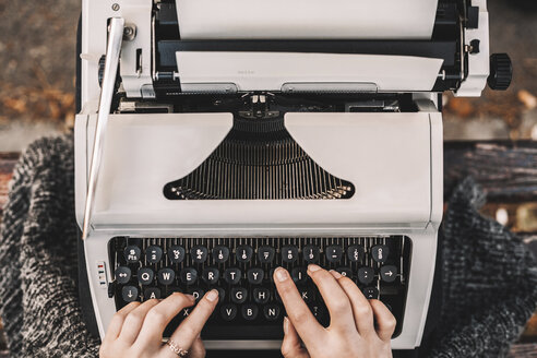 Ausgeschnittenes Bild einer Schriftstellerin, die auf einer Parkbank sitzend eine Schreibmaschine benutzt - CAVF57372