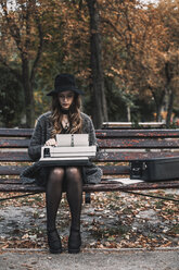 Schriftstellerin mit Schreibmaschine auf einer Parkbank sitzend im Herbst - CAVF57374