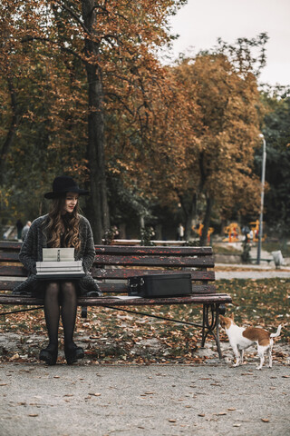 Schriftstellerin sieht Hund an, während sie auf einer Parkbank im Herbst Schreibmaschine schreibt, lizenzfreies Stockfoto