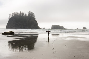 Rear view of silhouette woman with arms outstretched standing at beach in Olympic National Park - CAVF57380