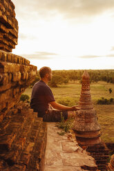 Seitenansicht eines meditierenden Mannes, der auf einem buddhistischen Tempel sitzt, gegen den Himmel bei Sonnenuntergang - CAVF57381