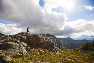 Hiker climbing on rocks against cloudy sky - CAVF57410