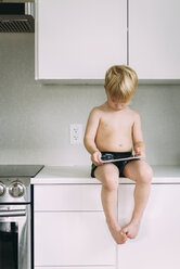 Hemdloser Junge, der einen Tablet-Computer benutzt, während er zu Hause auf dem Küchentisch sitzt - CAVF57415