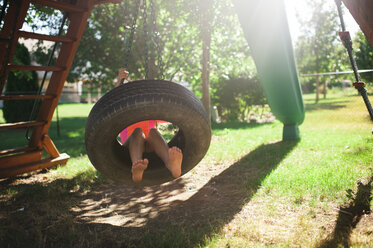 Low section of boy swinging in tire swing at playground - CAVF57418