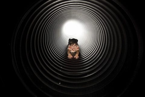 Porträt eines verspielten Jungen, der in einem riesigen Metallrohr liegt, lizenzfreies Stockfoto