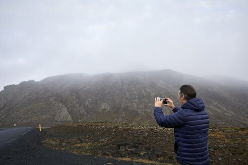 Rear view of man photographing while standing on road against sky - CAVF57431