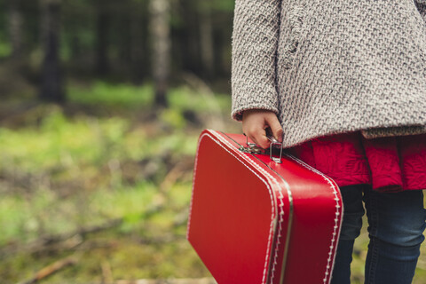 Midsection of girl with red briefcase standing at forest stock photo