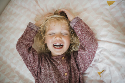 Draufsicht auf ein fröhliches, auf dem Bett liegendes Mädchen mit geschlossenen Augen, lizenzfreies Stockfoto