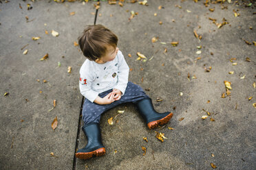 Hoher Blickwinkel auf einen kleinen Jungen, der im Herbst auf einem Fußweg sitzt - CAVF57463