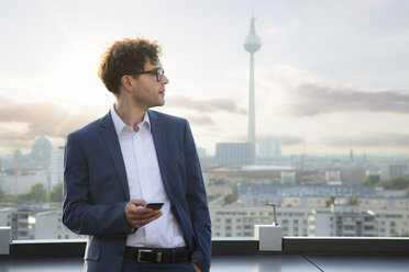 Deutschland, Berlin, Geschäftsmann mit Smartphone auf Dachterrasse am Abend - FKF03118