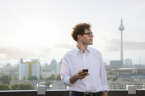 Deutschland, Berlin, zufriedener Geschäftsmann auf Dachterrasse mit Blick in die Ferne, lizenzfreies Stockfoto