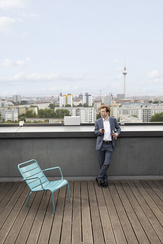 Deutschland, Berlin, Geschäftsmann entspannt auf Dachterrasse bei einem Getränk, lizenzfreies Stockfoto