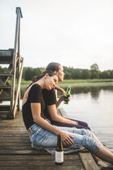 Seitenansicht von Freundinnen, die bei Sonnenuntergang auf dem Steg sitzen und auf den See blicken - MASF09700