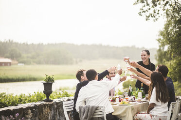 Fröhliche männliche und weibliche Freunde stoßen mit Weingläsern während einer Dinnerparty im Hinterhof an - MASF09713