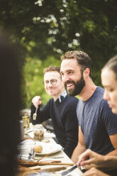 Lächelnder Mann, der wegschaut, während er eine Dinnerparty mit Freunden im Hinterhof genießt - MASF09715