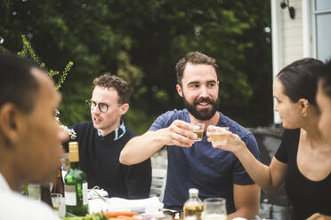 Mann und Frau stoßen mit Getränken an, während sie eine Dinnerparty mit Freunden im Hinterhof genießen - MASF09718