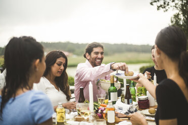 Male and female friends enjoying dinner during party in backyard - MASF09720