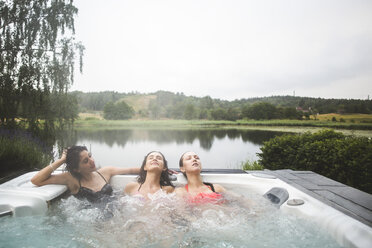 Weibliche Freunde genießen im Whirlpool mit geschlossenen Augen gegen See während Wochenendausflug - MASF09724
