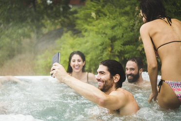 Young man taking selfie through mobile phone while friends enjoying in hot tub during weekend getaway - MASF09733