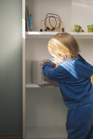 Kleines Mädchen nimmt Spielzeug aus dem Regal, lizenzfreies Stockfoto