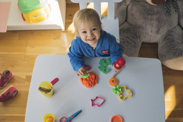 Porträt eines lächelnden kleinen Mädchens, das mit Knetmasse im Kinderzimmer spielt - MOMF00554