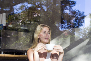 Porträt einer Frau in einem Cafe mit einer Tasse Kaffee, die aus dem Fenster schaut - LMJF00015