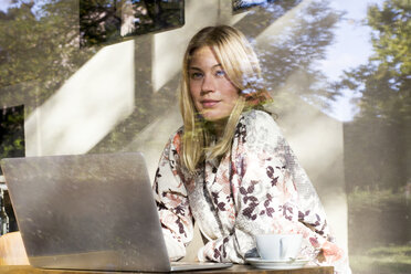 Porträt einer blonden Frau mit Laptop, die in einem Café sitzt und aus dem Fenster schaut - LMJF00016