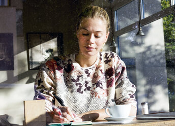 Porträt einer Frau in einem Café, die in ein Notizbuch schreibt - LMJF00020