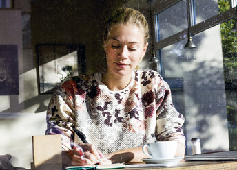 Portrait of woman in a cafe writing on notebook - LMJF00020