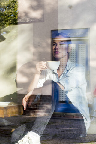 Frau sitzt in einem Café und trinkt eine Tasse Kaffee, während sie aus dem Fenster schaut, lizenzfreies Stockfoto