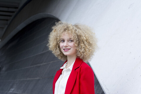 Porträt einer lächelnden blonden Frau mit Locken im roten Anzug, lizenzfreies Stockfoto