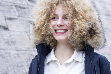 Portrait of laughing blond woman with ringlets wearing fur hood - LMJF00053