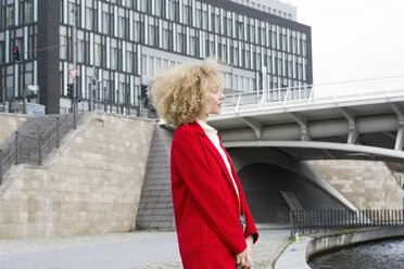 Deutschland, Berlin, blonde junge Frau mit Locken und rotem Mantel - LMJF00056