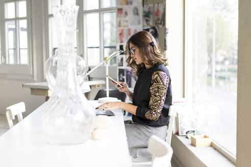 Junge Designerin mit Smartphone in ihrem Atelier - AFVF02046
