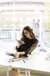 Smiling young designer looking at smartphone in an atelier - AFVF02048