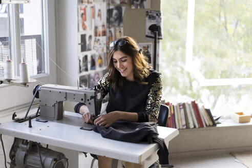 Lächelnde junge Modedesignerin an der Nähmaschine in ihrem Atelier - AFVF02054