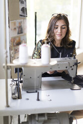 Porträt einer jungen Designerin an der Nähmaschine in ihrem Atelier - AFVF02055