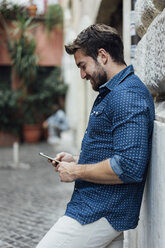 Bearded man leaning against facade looking at cell phone - BOYF01073