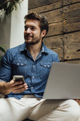 Smiling businessman with laptop and smartphone outdoors - BOYF01096