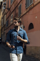 Portrait of businessman with smartphone and earphones on the street - BOYF01105