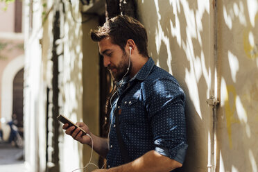 Man using earphones and smartphone outdoors - BOYF01113